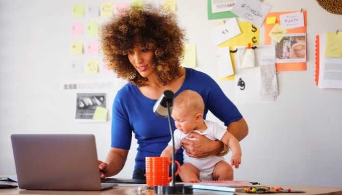 Mãe segurando bebê enquanto trabalha.